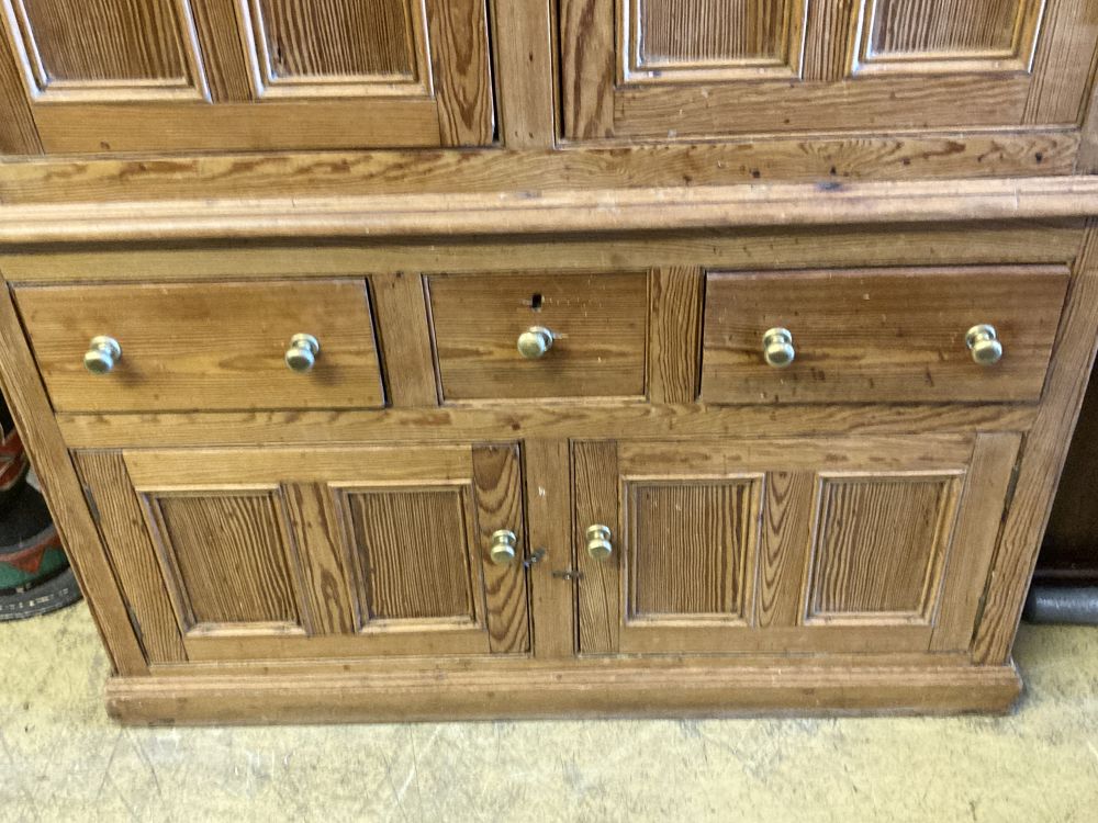 An early 19th century stripped pine cupboard, fitted with a pair of part glazed panelled doors, over three drawers and cupboards, width